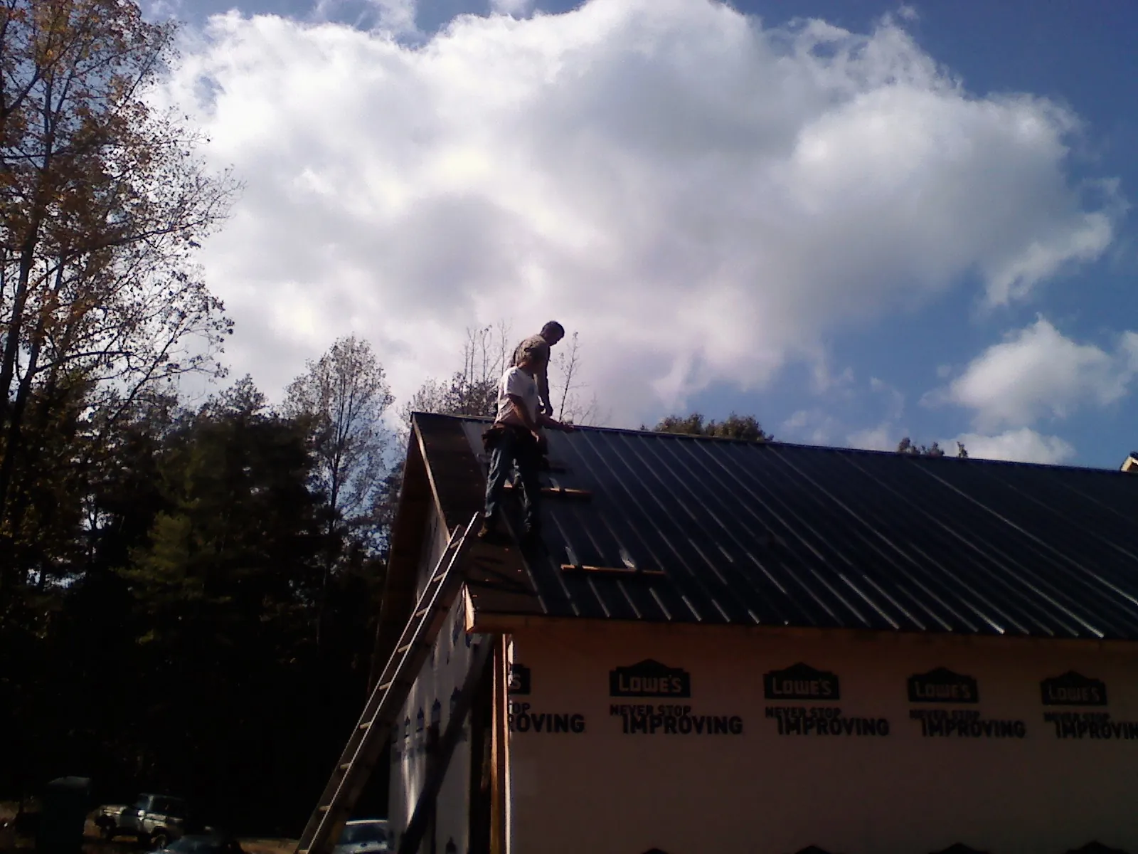 Roofer fastening dark metal panels high against a cloudy sky, from a Roof Inspection job in Windber