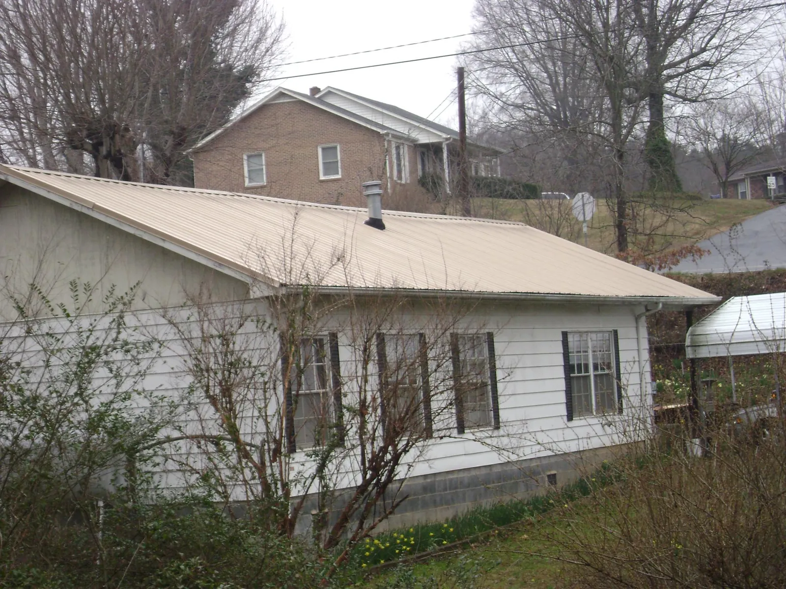 Tan metal roof on a white sided house set into a hillside — Commercial Roofing by Roofing Brothers in Windber